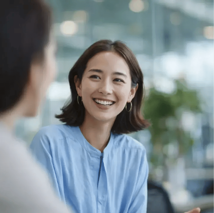 Professional Asian woman smiling during office conversation wearing light blue shirt and gold hoop earrings