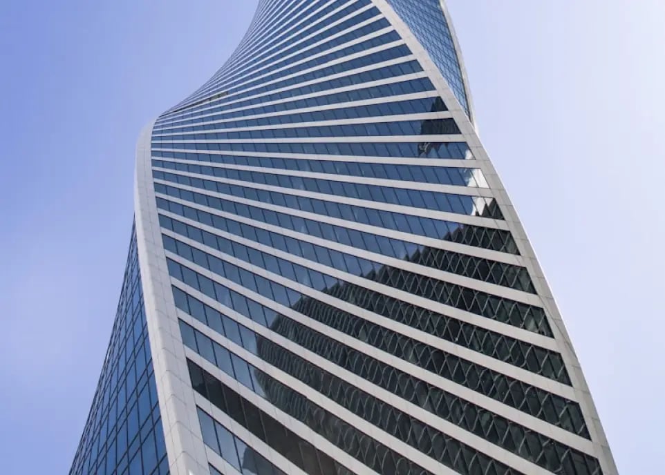 Modern twisted skyscraper with glass facade and horizontal white bands spiraling upward against blue sky