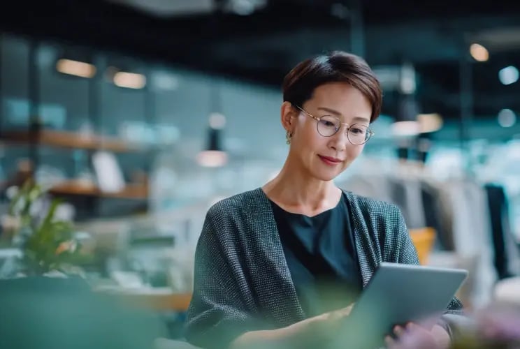 Professional Asian woman in glasses reviewing trust documents on tablet in modern office