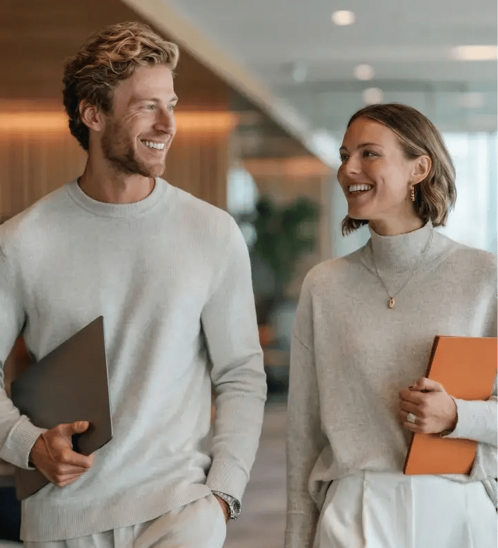 Two corporate professionals smiling while walking through modern office with folders discussing business services
