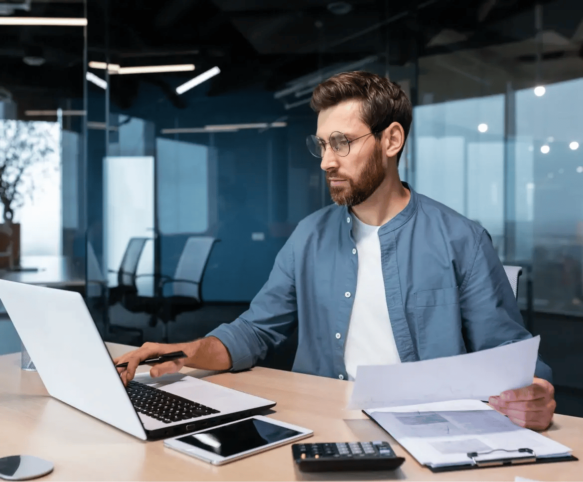 Professional director reviewing compliance documents at laptop in modern corporate office