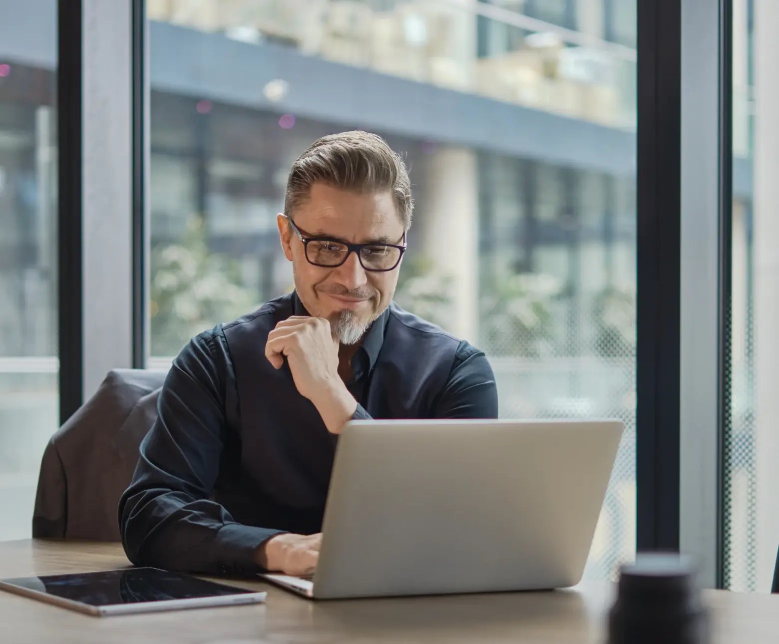 Professional businessman in glasses reviewing trademark registration documents on laptop in modern office