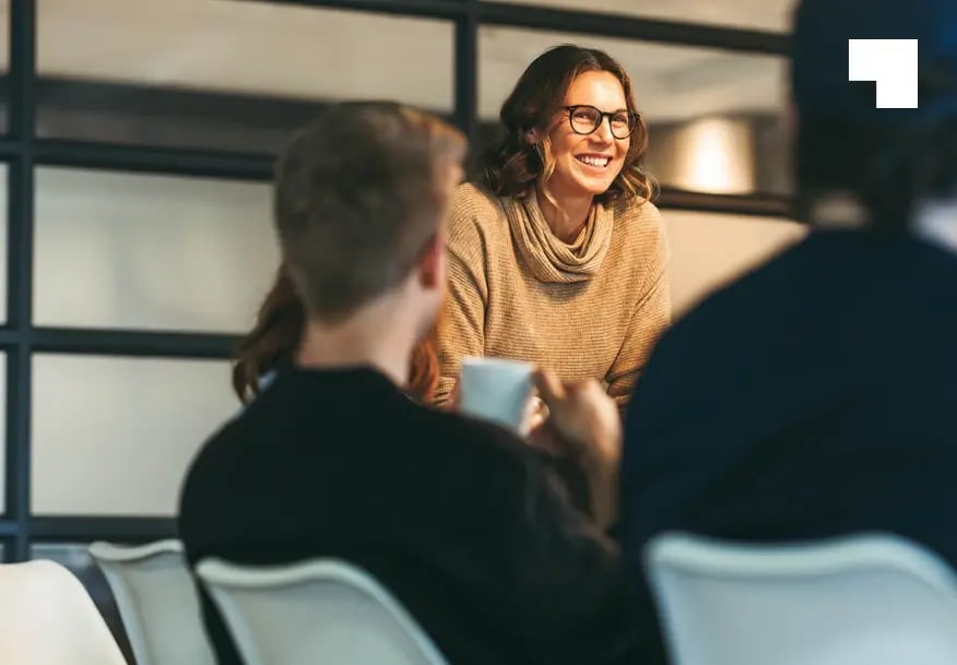 Professional woman in beige sweater smiling during business consultation meeting with clients in modern office