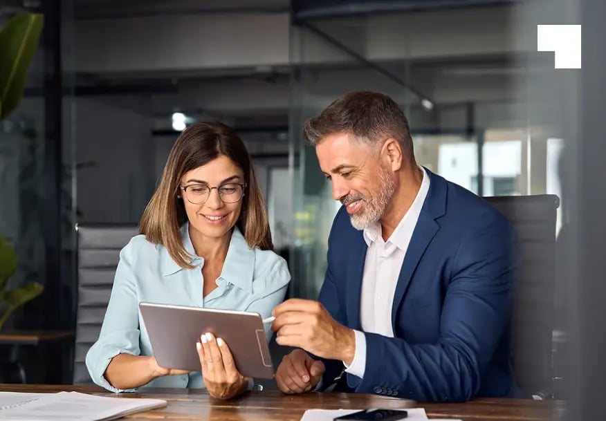Two business professionals reviewing compliance documents on tablet in modern office