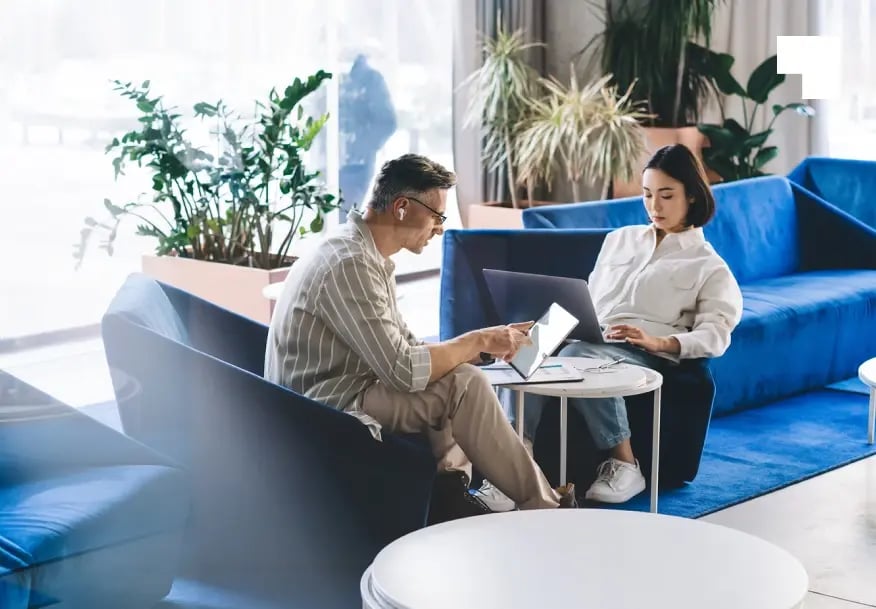Two professionals collaborating with laptops at modern office, discussing share registry and client services